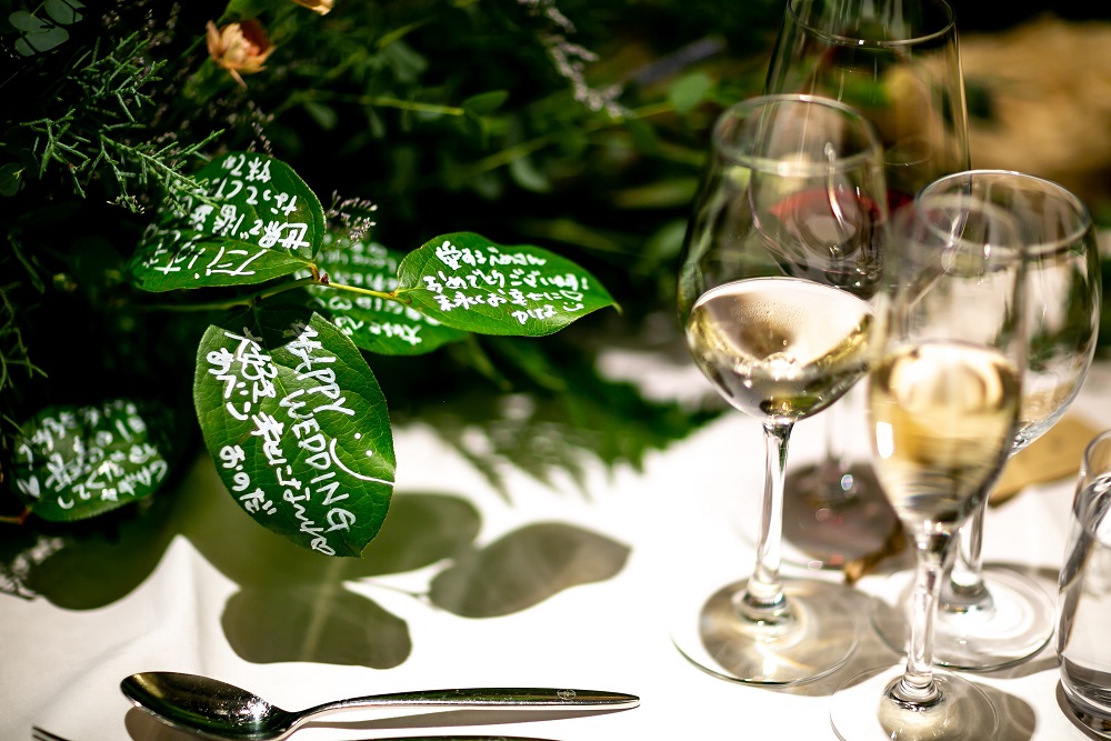 ゲストテーブルのお花にあしらったグリーンにゲストからおふたりへメッセージを記入する楽しい試みがあったりとおふたりのアイデアが光ります。