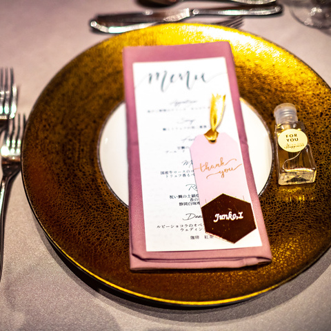 結婚式のテーマカラーであるゴールドと、ピンクを基調とした テーブルコーディネートは、 全て新婦様の手が込んだアイテムに。 メニュー表やミラー席札、アルコールジェルも添えて・・・ 新婦様のゲストへの心配りとセンスが光ります。